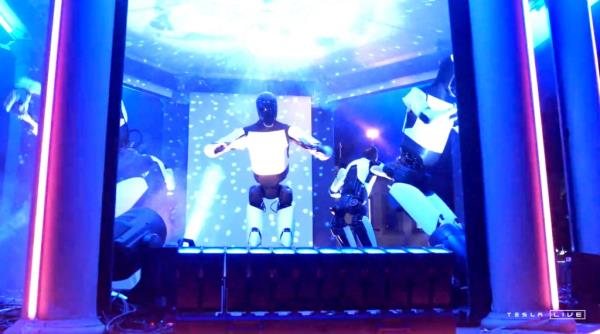 Tesla Optimus robots dance onstage with a disco ball, colorful lights and a fog machine at event on Oct. 10, 2024.